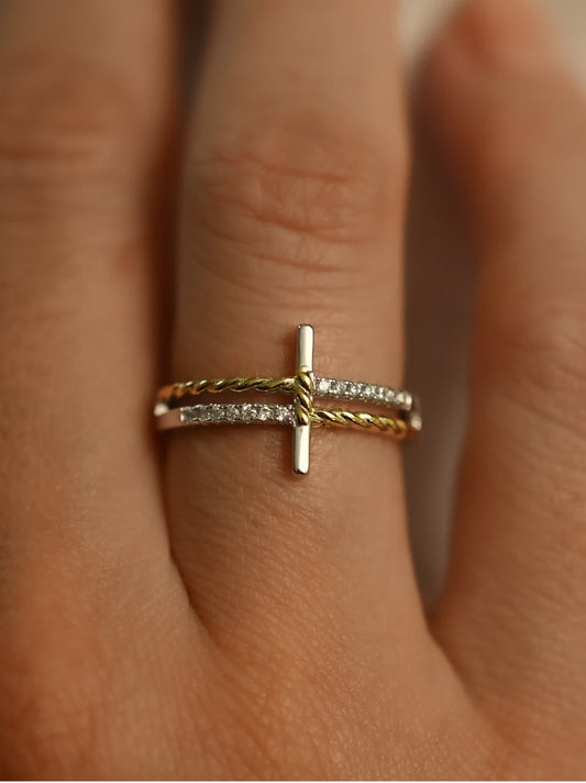 Close-up of two-tone silver and gold cross ring worn on finger, highlighting elegant wrap design and symbolic vertical cross shape