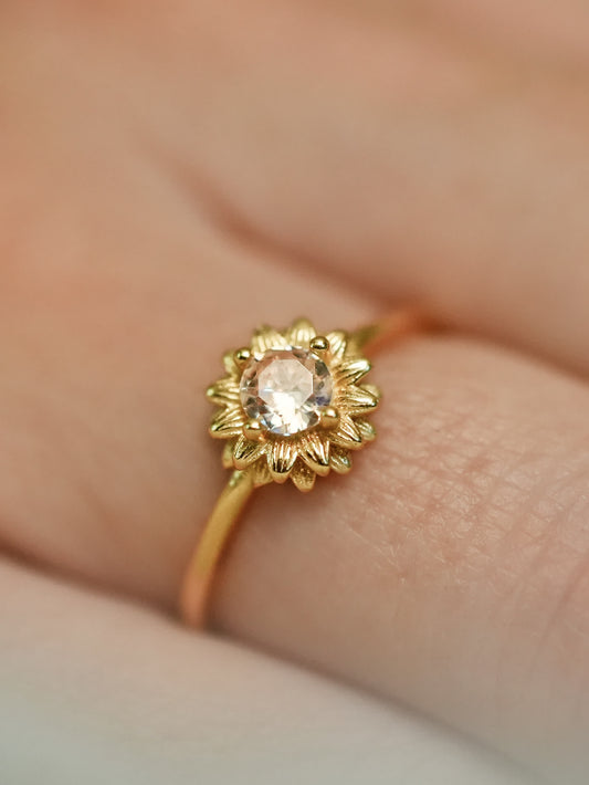Close-up of the sunflower gold ring worn on a woman's finger, showing the intricate petal texture and brilliant yellow center stone