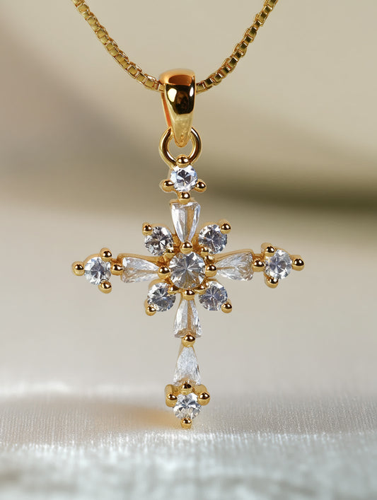 Close-up of gold starburst cross necklace with crystal bloom design, photographed on soft white fabric