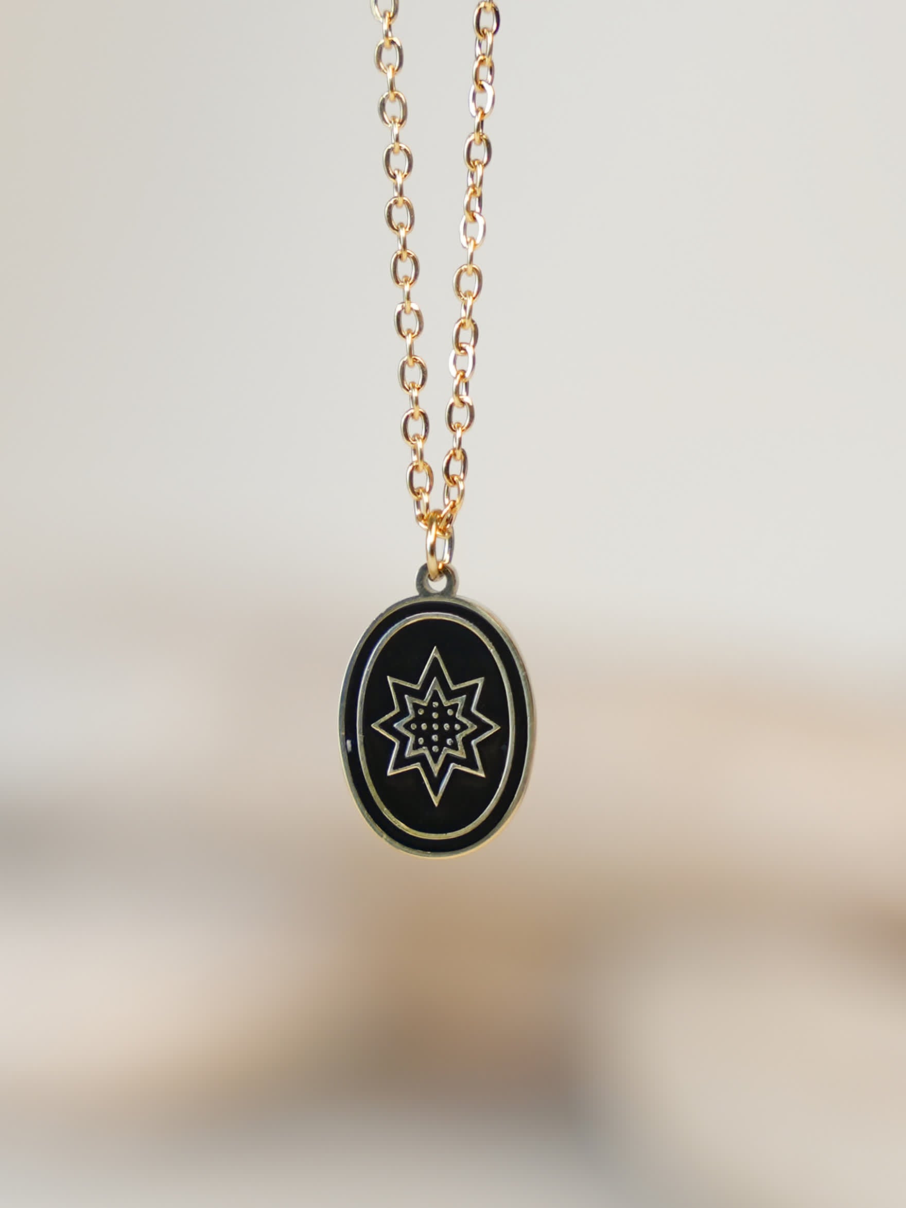 Close-up of black enamel star pendant with gold detailing hanging against light background