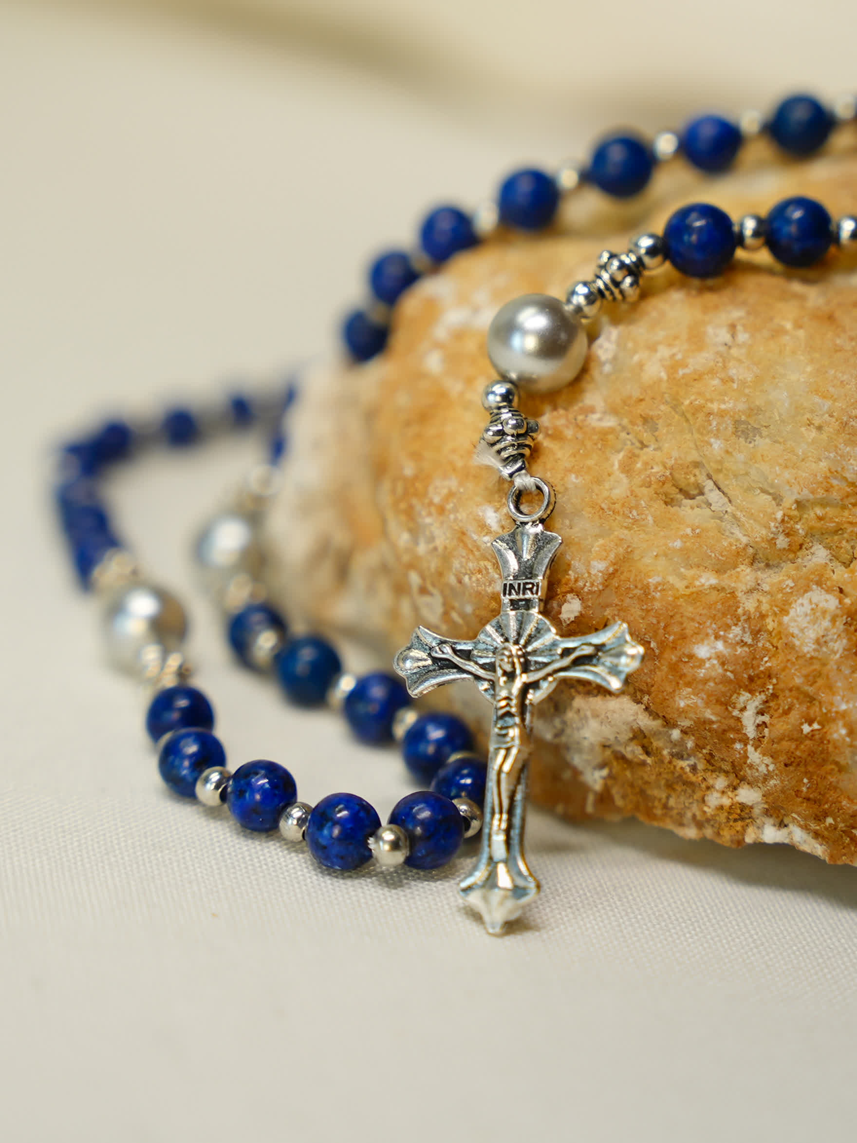 Lapis lazuli rosary necklace with silver crucifix laid beside artisan bread on soft fabric