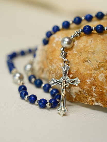 Lapis lazuli rosary necklace with silver crucifix laid beside artisan bread on soft fabric