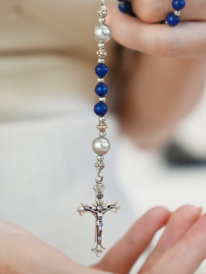 Detailed view of silver crucifix and pearl centerpiece on blue gemstone rosary necklace