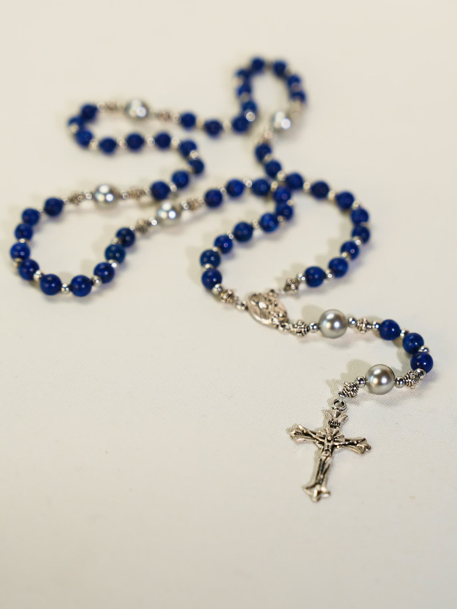 Lapis lazuli rosary necklace with silver crucifix and pearl accents arranged on a white surface