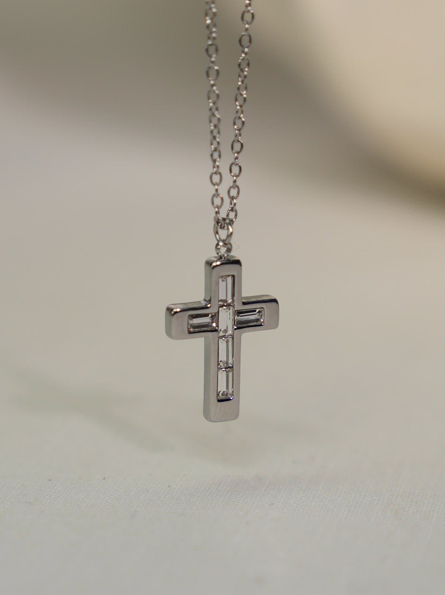 Steel cross necklace with geometric baguette stones suspended against a stone backdrop