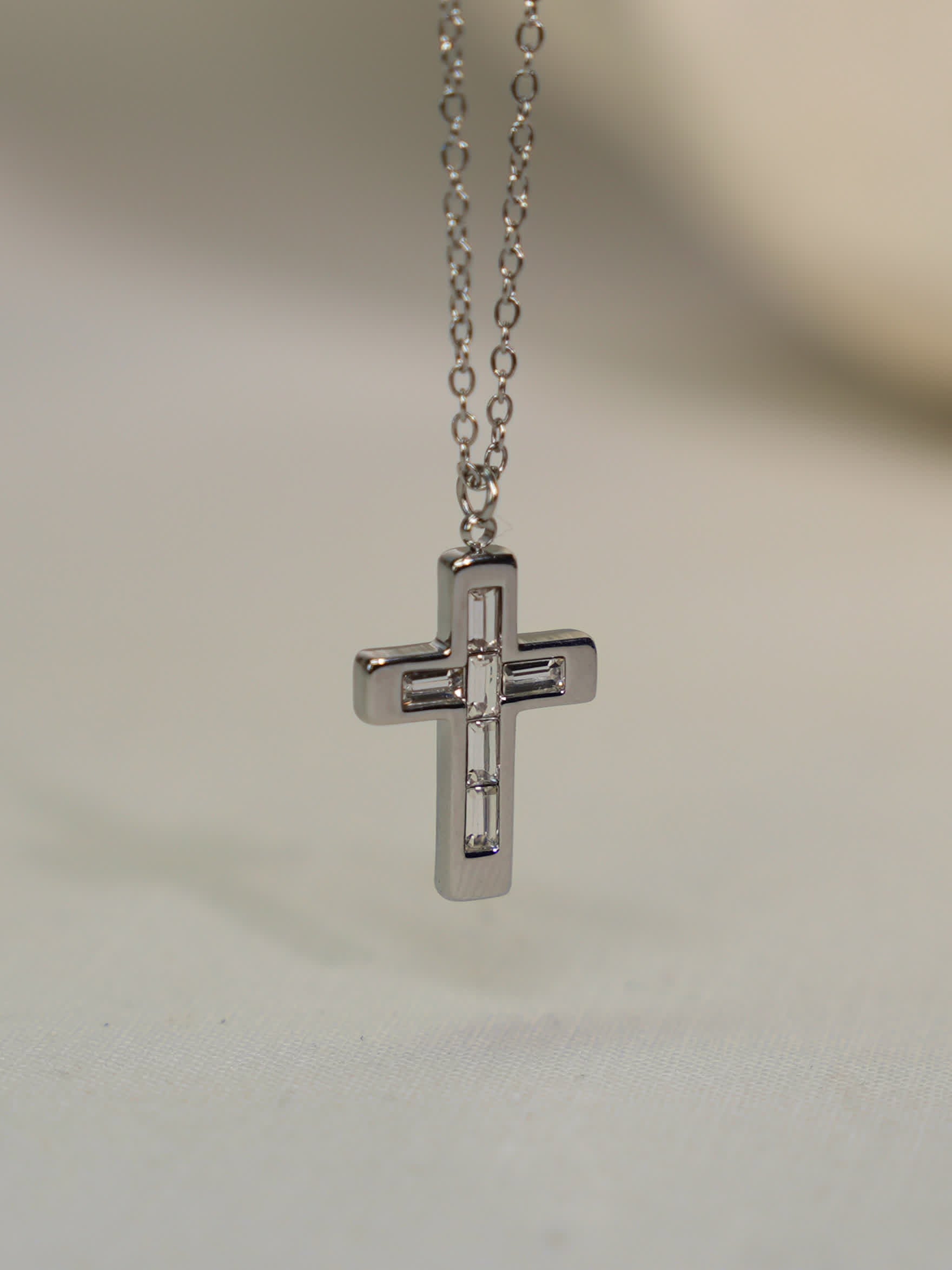 Steel cross necklace with geometric baguette stones suspended against a stone backdrop