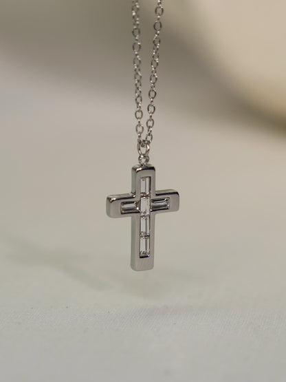 Steel cross necklace with geometric baguette stones suspended against a stone backdrop