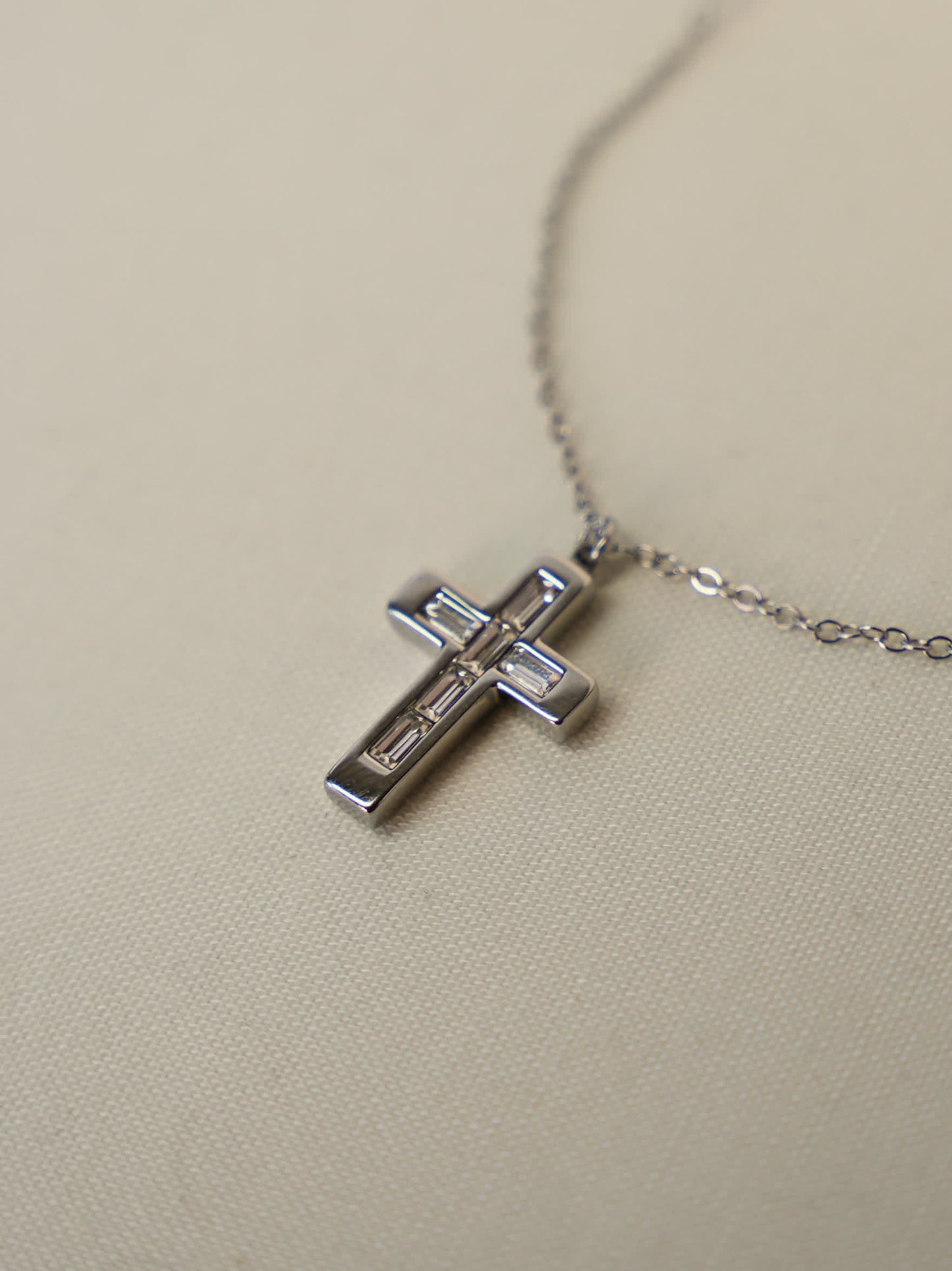 Close-up of baguette zircon cross pendant lying on cream fabric