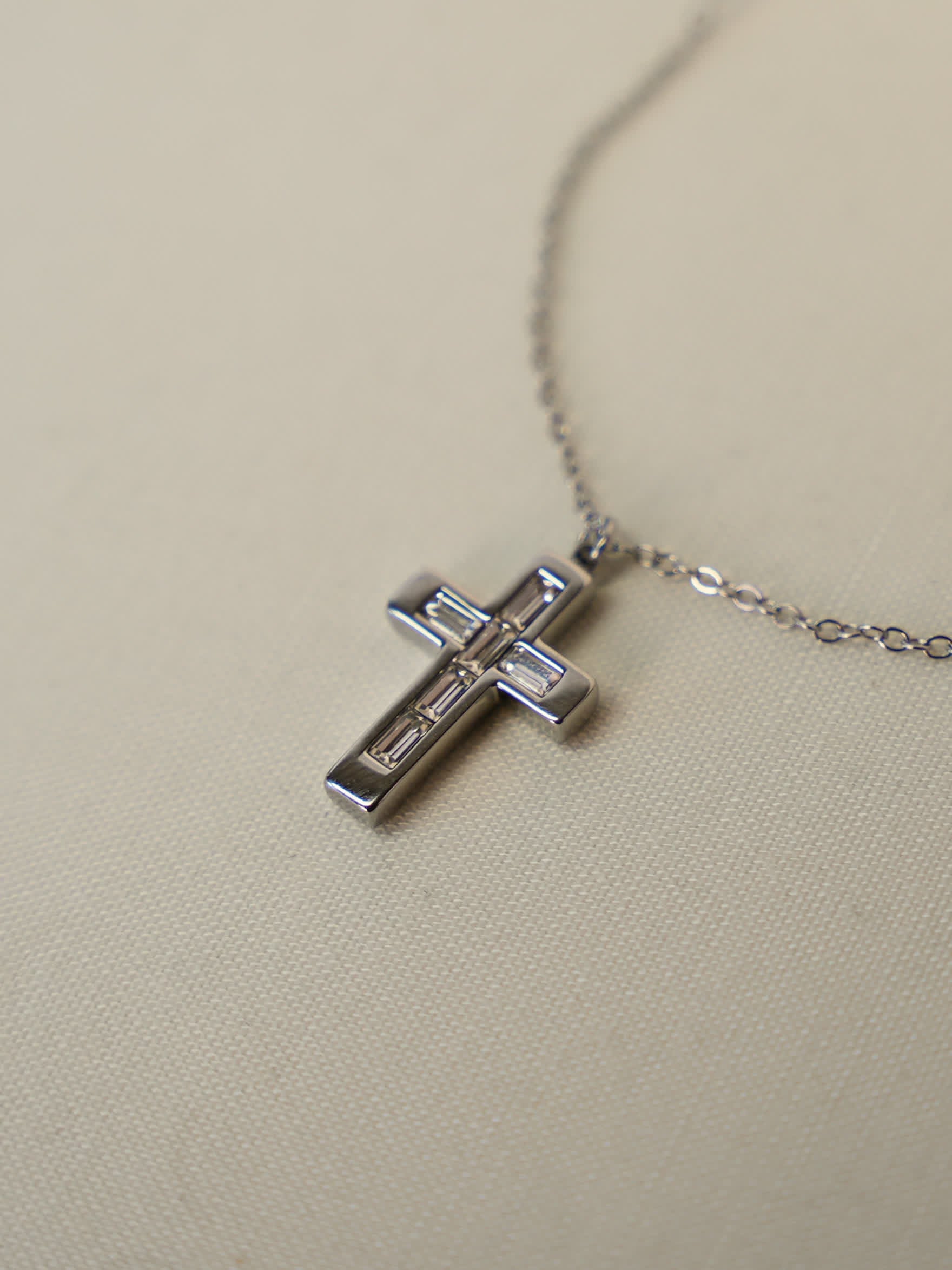 Close-up of baguette zircon cross pendant lying on cream fabric