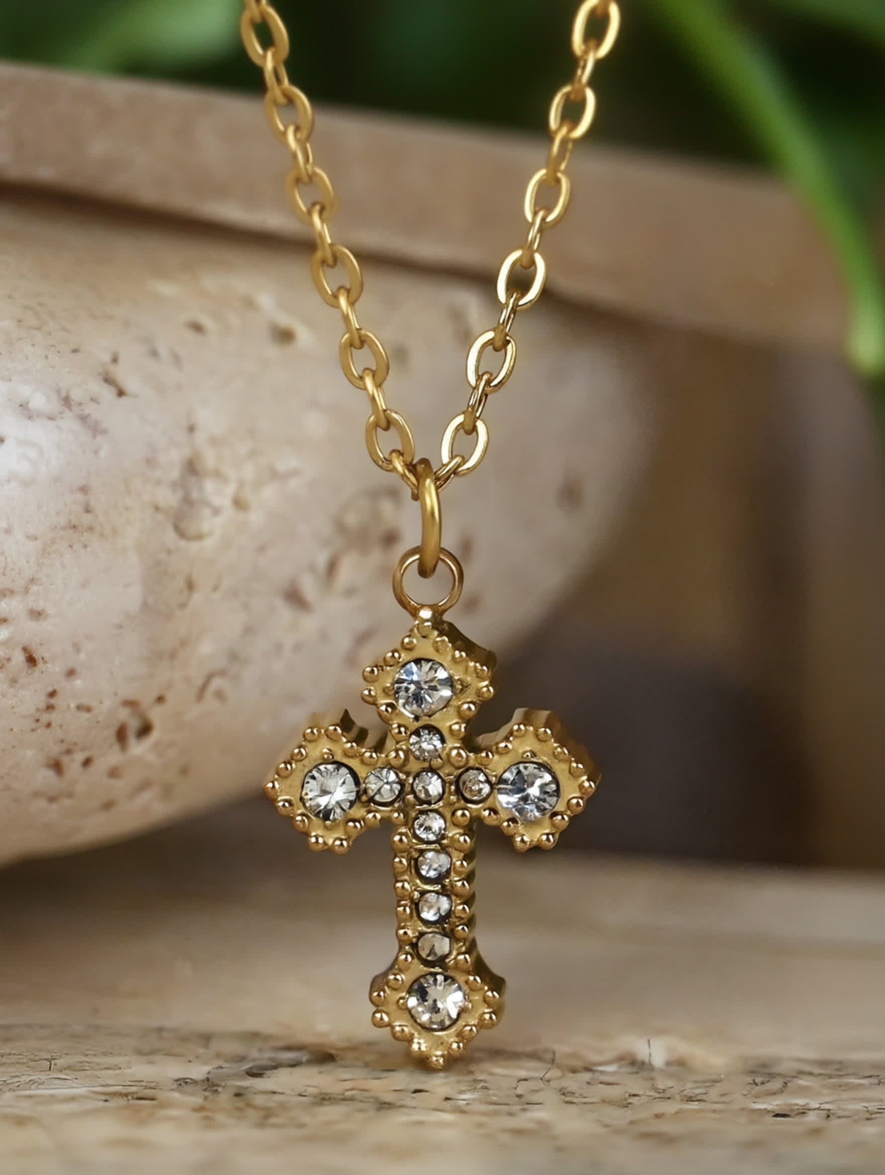 Gold Catholic cross necklace with sparkling stones hanging from ceramic backdrop