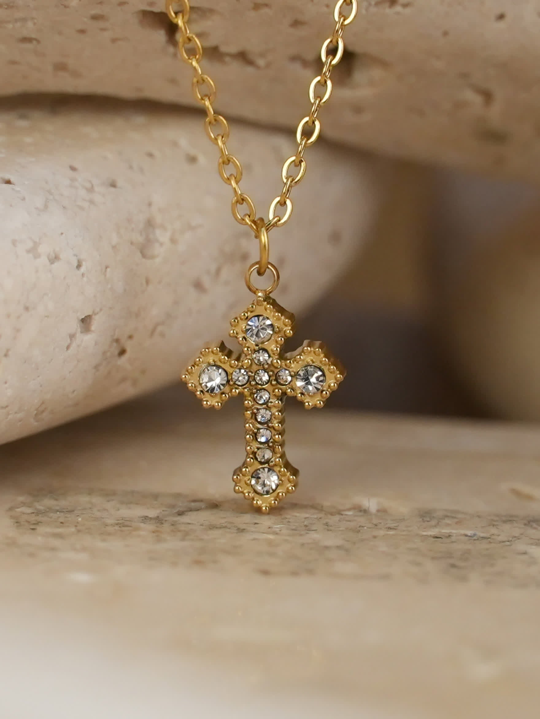 Close-up of gold Catholic cross pendant with zircon stones resting on travertine stone