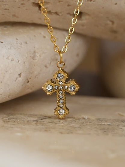 Close-up of gold Catholic cross pendant with zircon stones resting on travertine stone