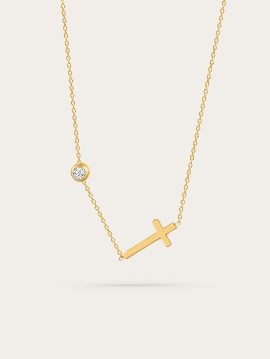 Sideways cross gold necklace with bezel-set zircon on light background
