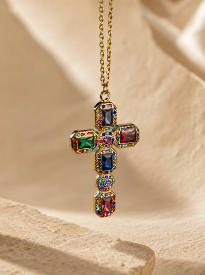 Multicolored gemstone cross pendant on a gold chain against a beige background