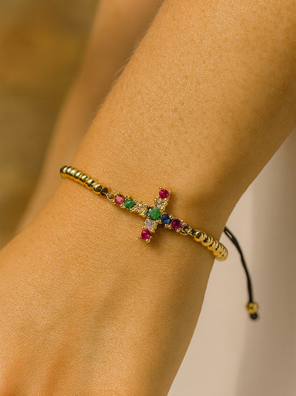 Lifestyle photo of the Joy in Light Cross Bracelet worn on a woman’s wrist, displaying the gold beaded band and rainbow-colored cross against warm natural lighting.