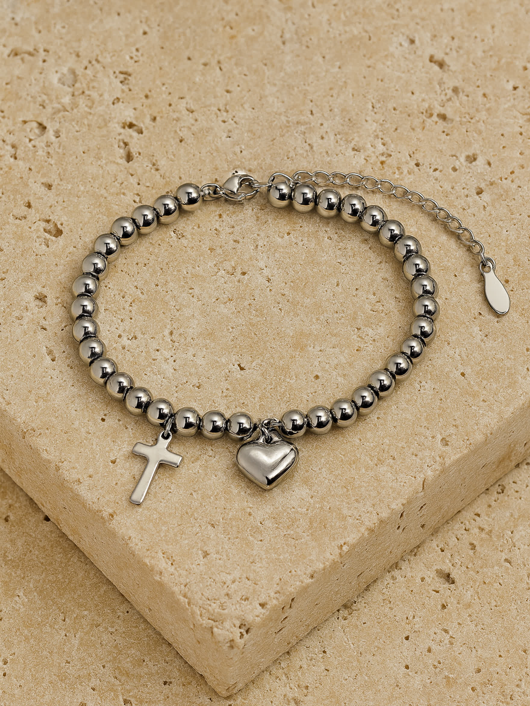 Lifestyle photo of the Pray Through It Cross Charm Bracelet worn on a woman’s wrist, displaying the heart and cross charms as a subtle, spiritual accent.