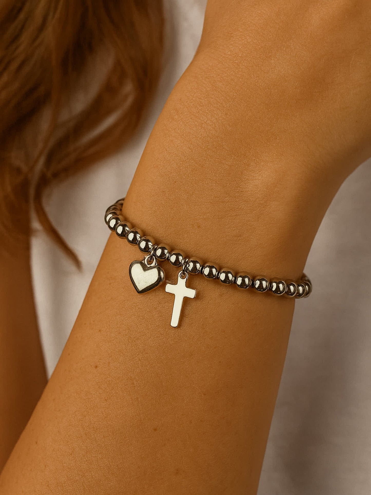 Overhead product shot of the Pray Through It Cross Charm Bracelet placed on a travertine block, showcasing the bracelet’s round bead structure and lobster clasp extender.