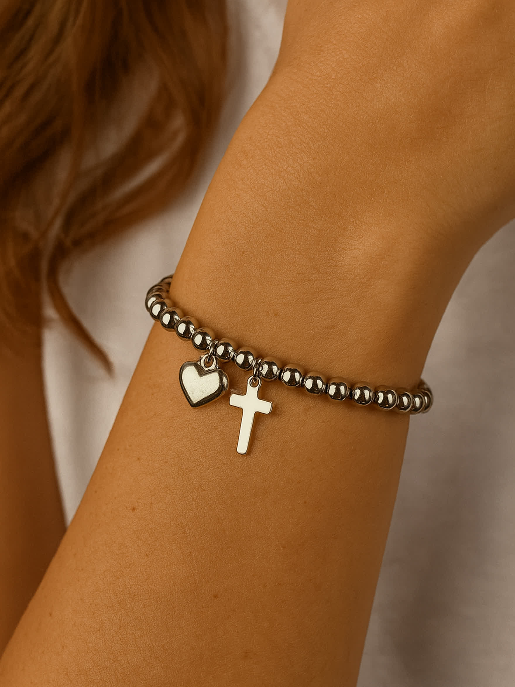 Overhead product shot of the Pray Through It Cross Charm Bracelet placed on a travertine block, showcasing the bracelet’s round bead structure and lobster clasp extender.
