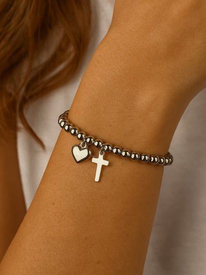 Overhead product shot of the Pray Through It Cross Charm Bracelet placed on a travertine block, showcasing the bracelet’s round bead structure and lobster clasp extender.