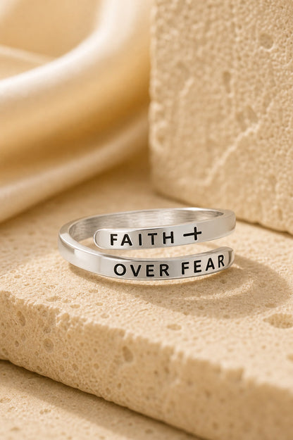 Silver ring with 'Faith Over Fear' engraving on a beige surface