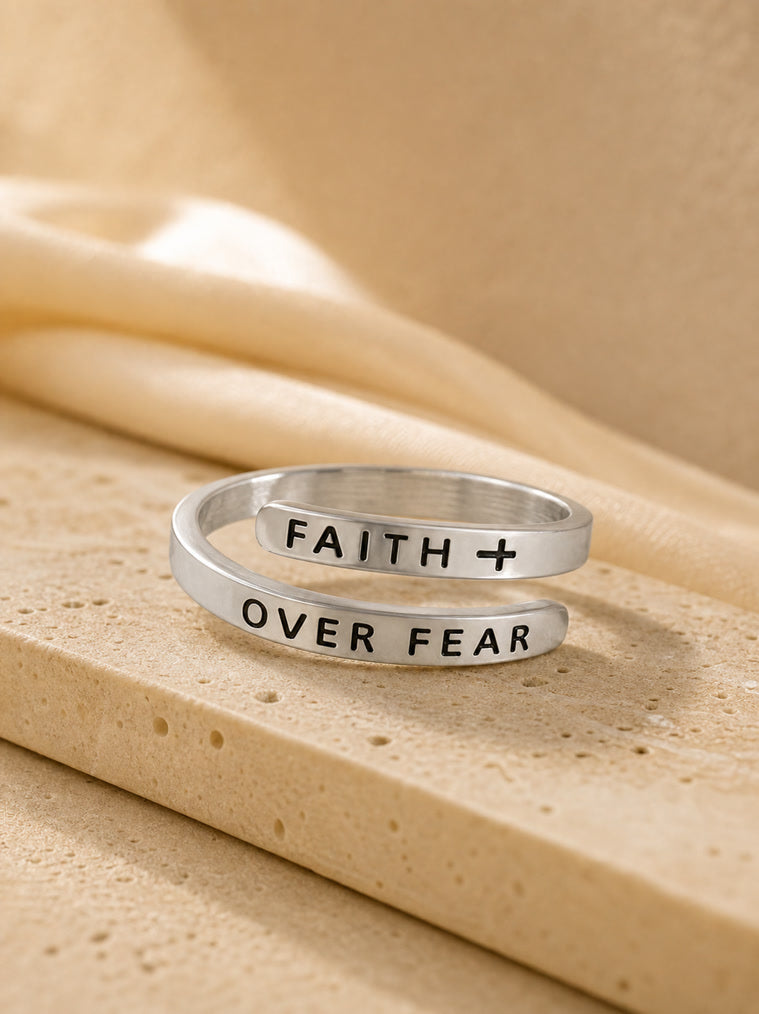Silver ring with 'FAITH OVER FEAR' engraving on a beige fabric background