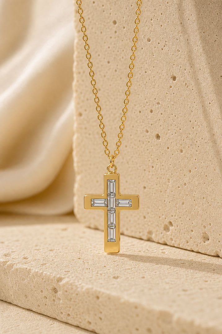 Gold cross necklace with clear stones on a beige fabric background