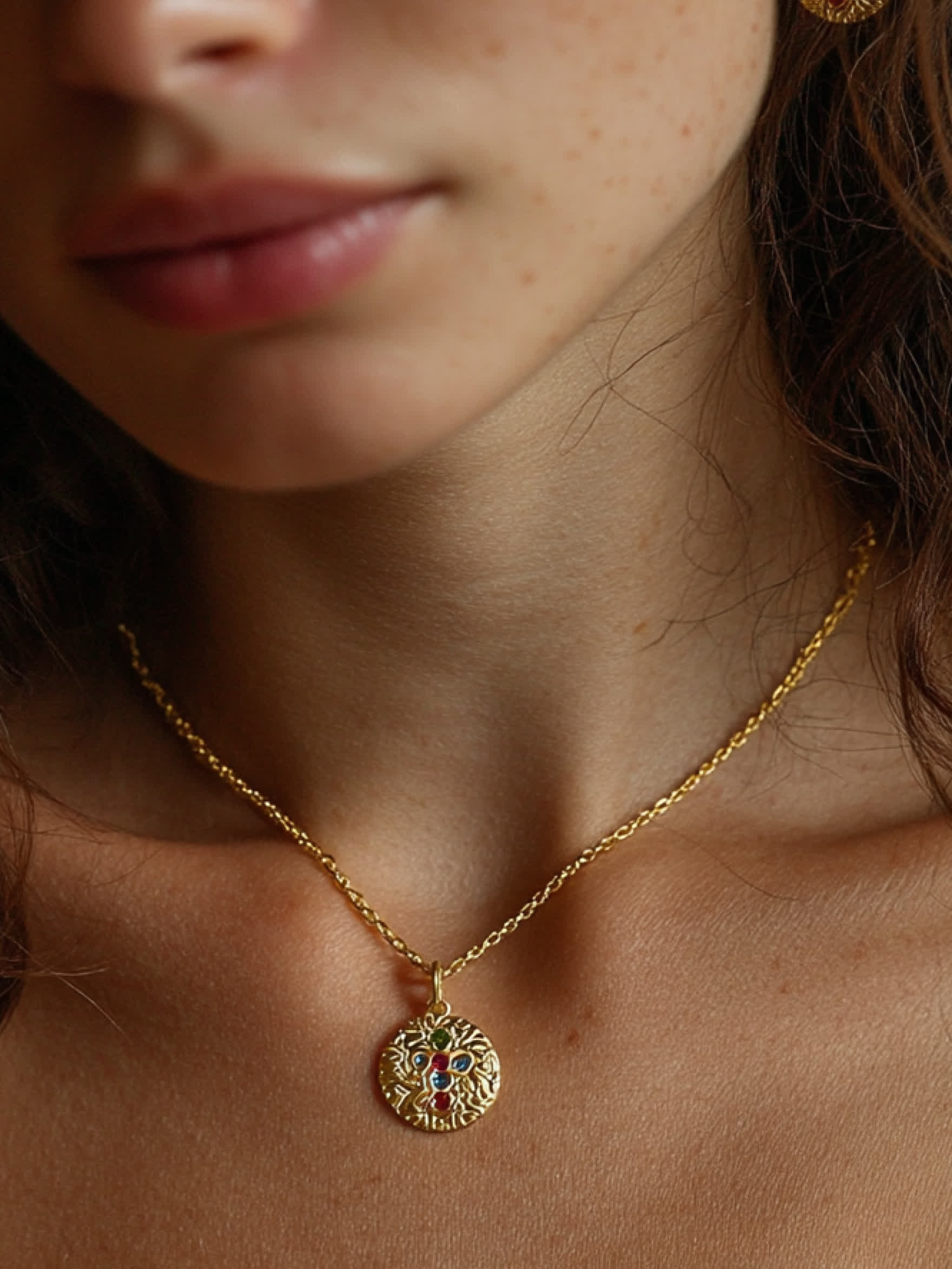Woman wearing colorful cross necklace with gold medallion at neckline