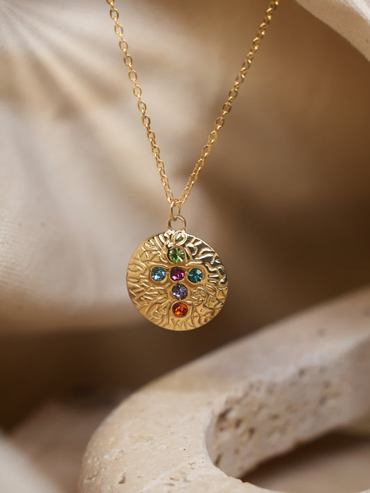 Multicolor gemstone cross pendant displayed on beige stone surface