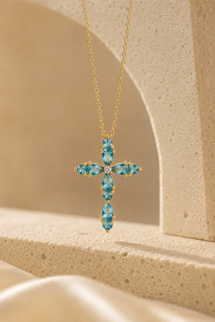 Gold cross necklace with blue gemstones on a beige background