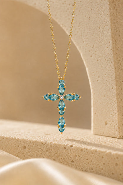 Gold cross necklace with blue gemstones on a beige background