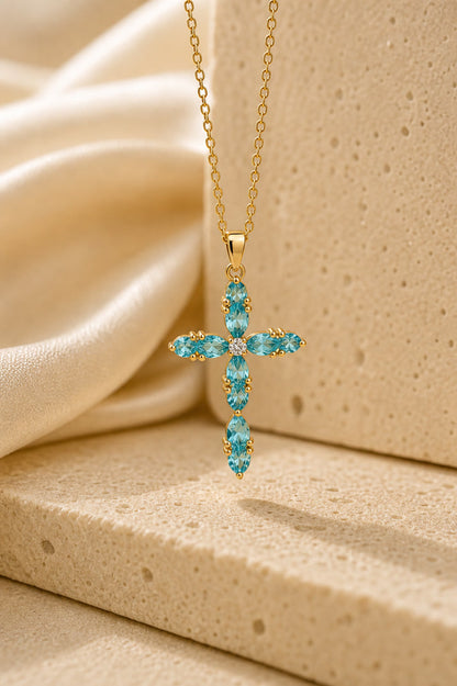 Gold cross necklace with blue gemstones on a beige fabric background