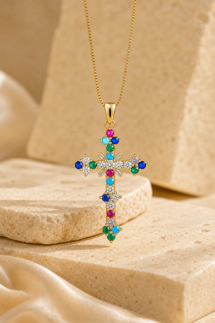Gold cross necklace with colorful gemstones on a beige stone surface