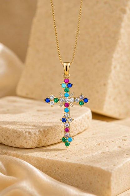 Gold cross necklace with colorful gemstones on a beige stone surface