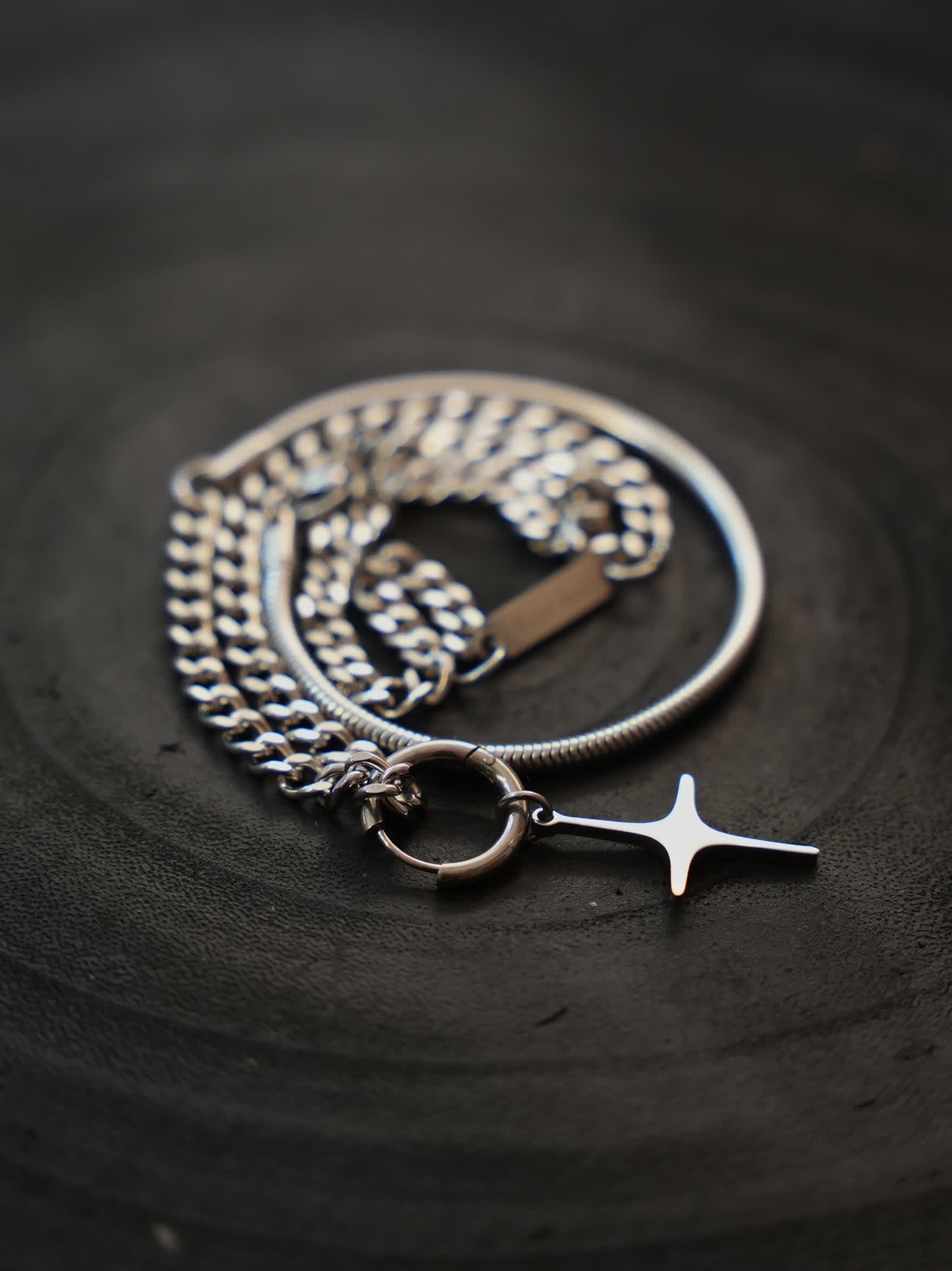 Contemporary stainless steel cross necklace coiled neatly beside its ringed bail on a black ceramic surface, showcasing sculptural elegance.