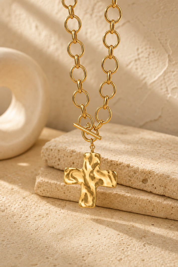 Gold chain necklace with a cross pendant on a beige stone surface