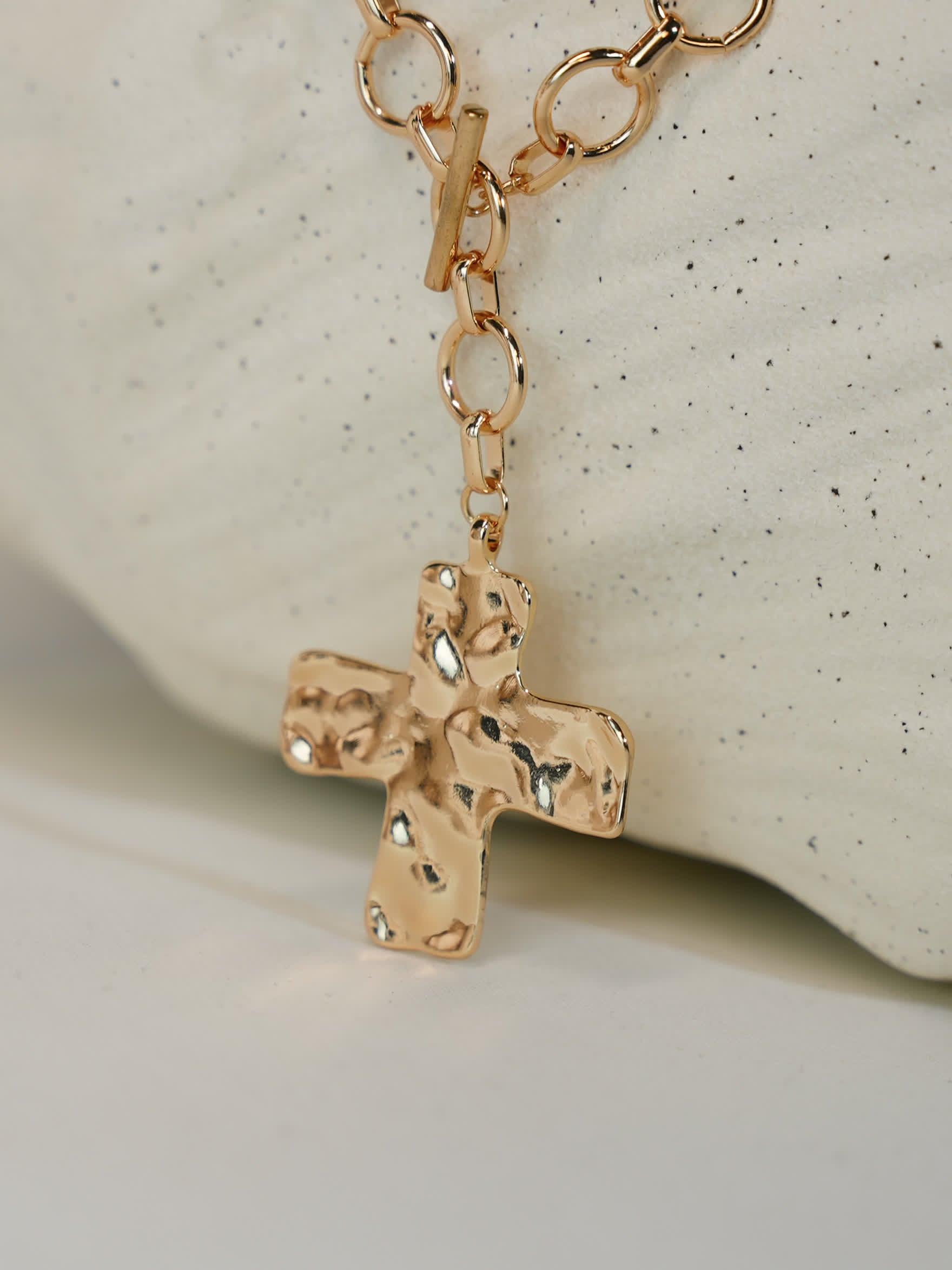 Close-up of hammered gold cross pendant with toggle clasp on minimalist display stone