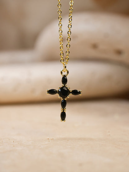 Front-facing image of black and gold cross necklace suspended over travertine surface