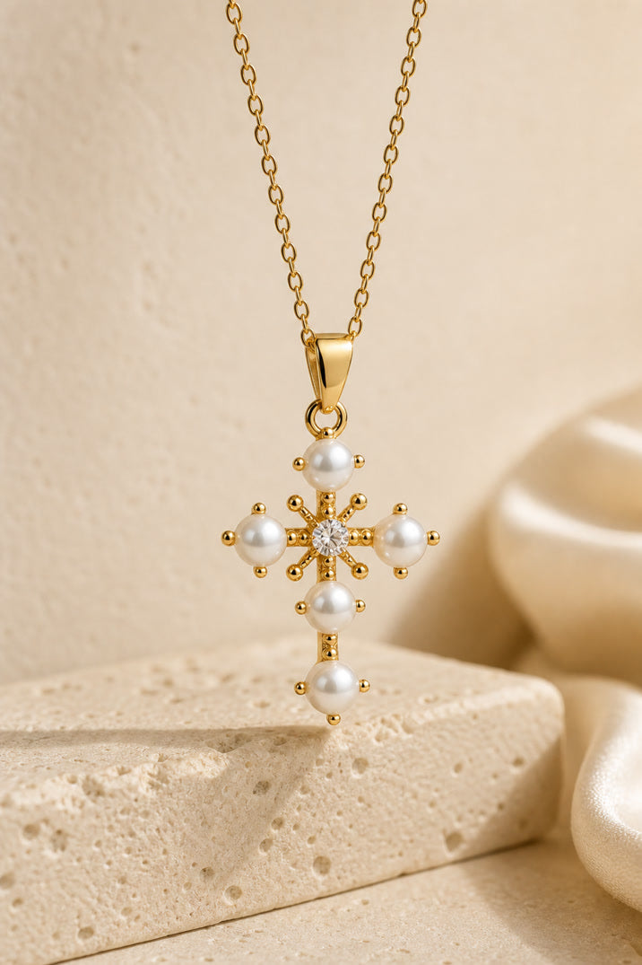 Gold necklace with a cross pendant featuring pearls on a beige background