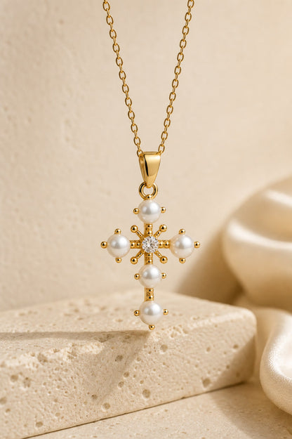 Gold necklace with a cross pendant featuring pearls on a beige background