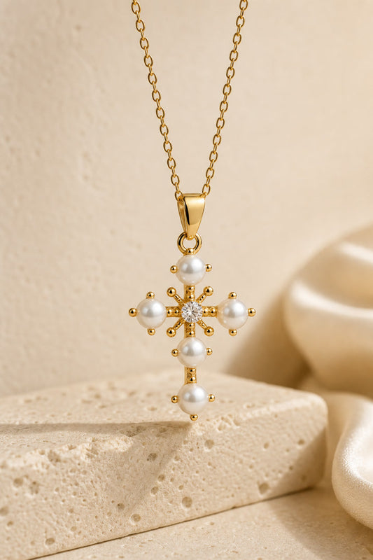 Gold necklace with a cross pendant featuring pearls on a beige background
