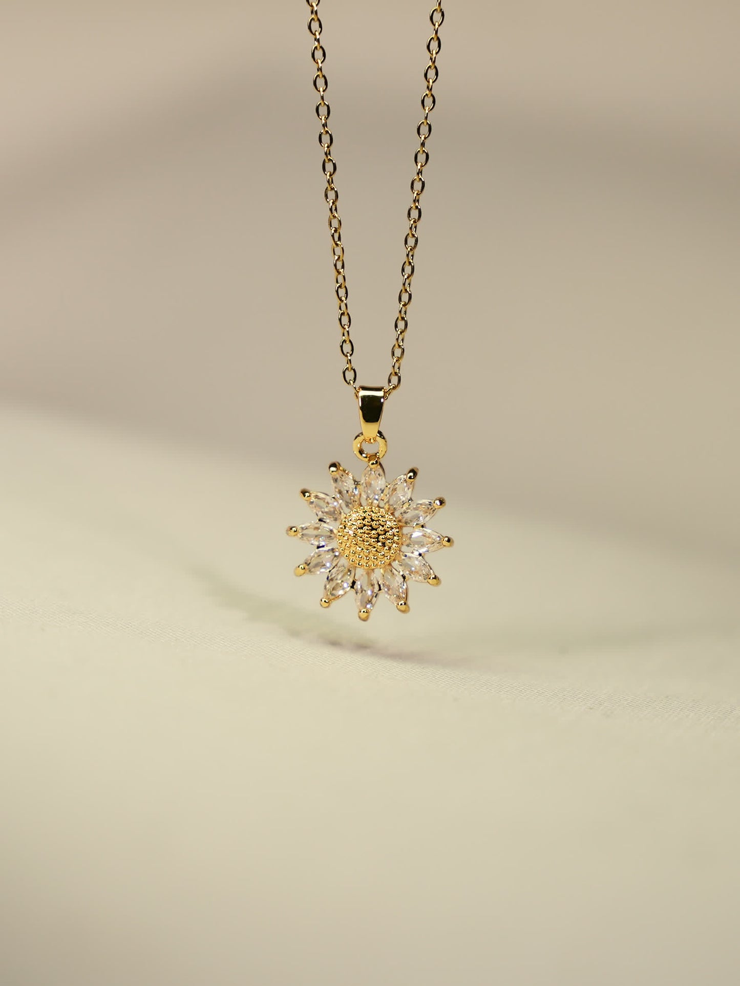 Gold-plated sunflower pendant with sparkling zircon stones photographed on soft beige fabric