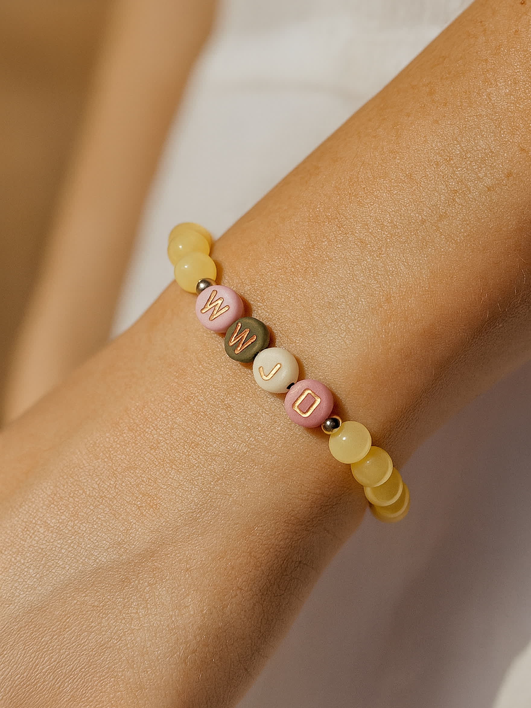 Lifestyle photo of the WWJD Bracelet worn on a woman's wrist, featuring pastel gemstone beads and WWJD letters in pink, white, and gold.